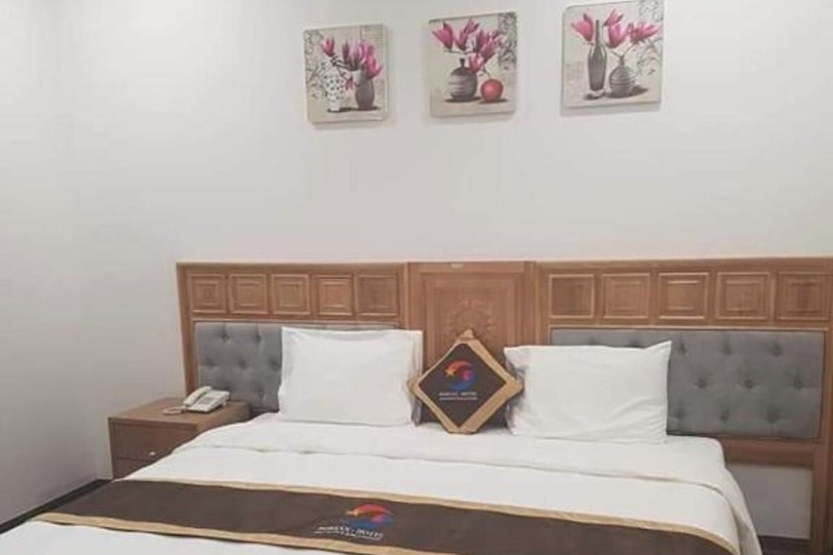 A hotel room with a large bed, two nightstands, a wooden headboard, and three wall-mounted paintings.