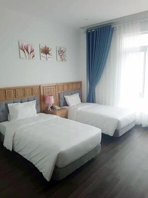 A hotel room with two beds, a wooden headboard, a nightstand with a lamp, and artwork on the wall. - Korea 2 Hotel (Bac Giang)
