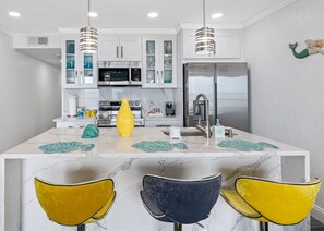 A modern kitchen with white cabinets, a stainless steel refrigerator, and a marble countertop.