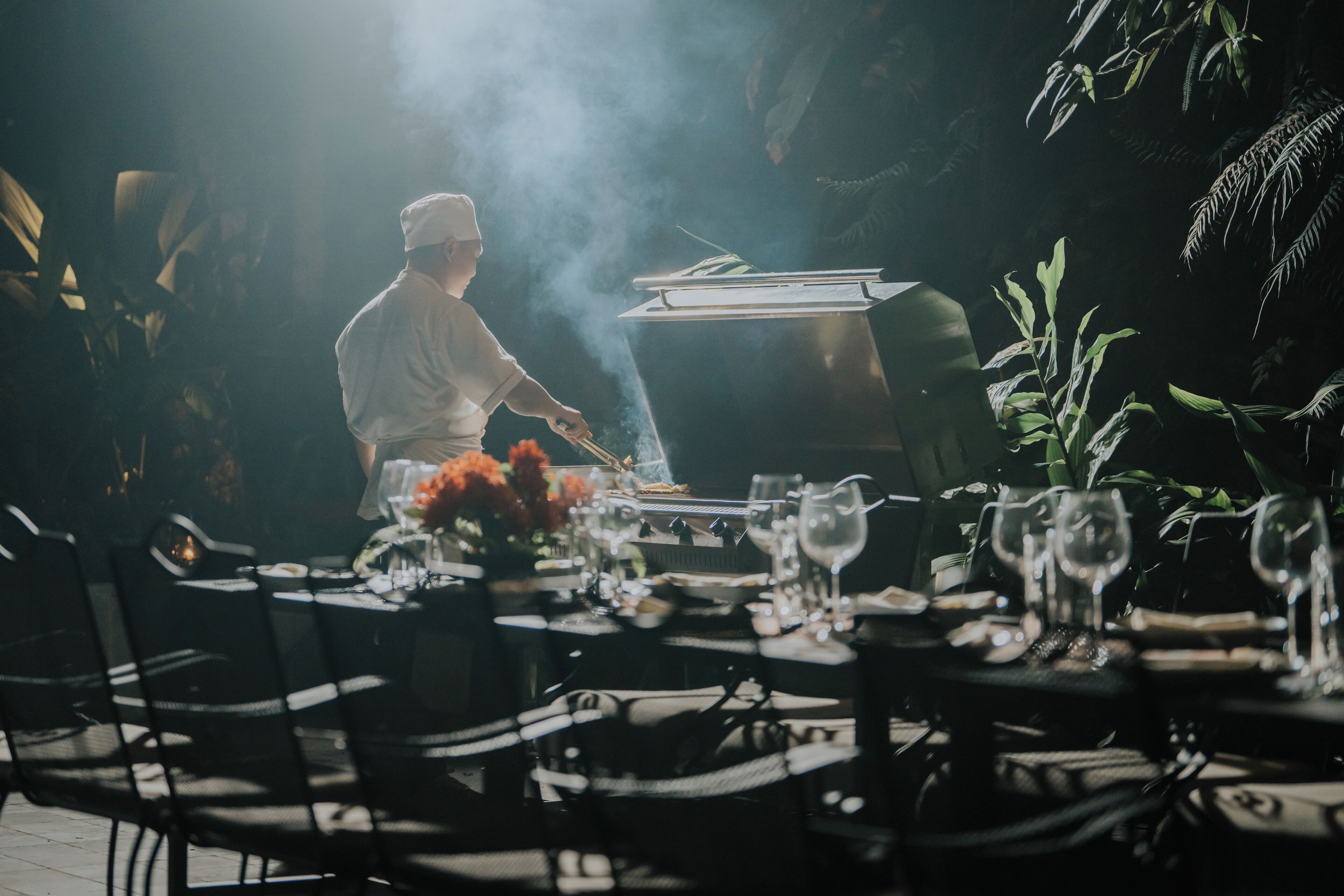 A chef grilling outdoors with a table set for dining.