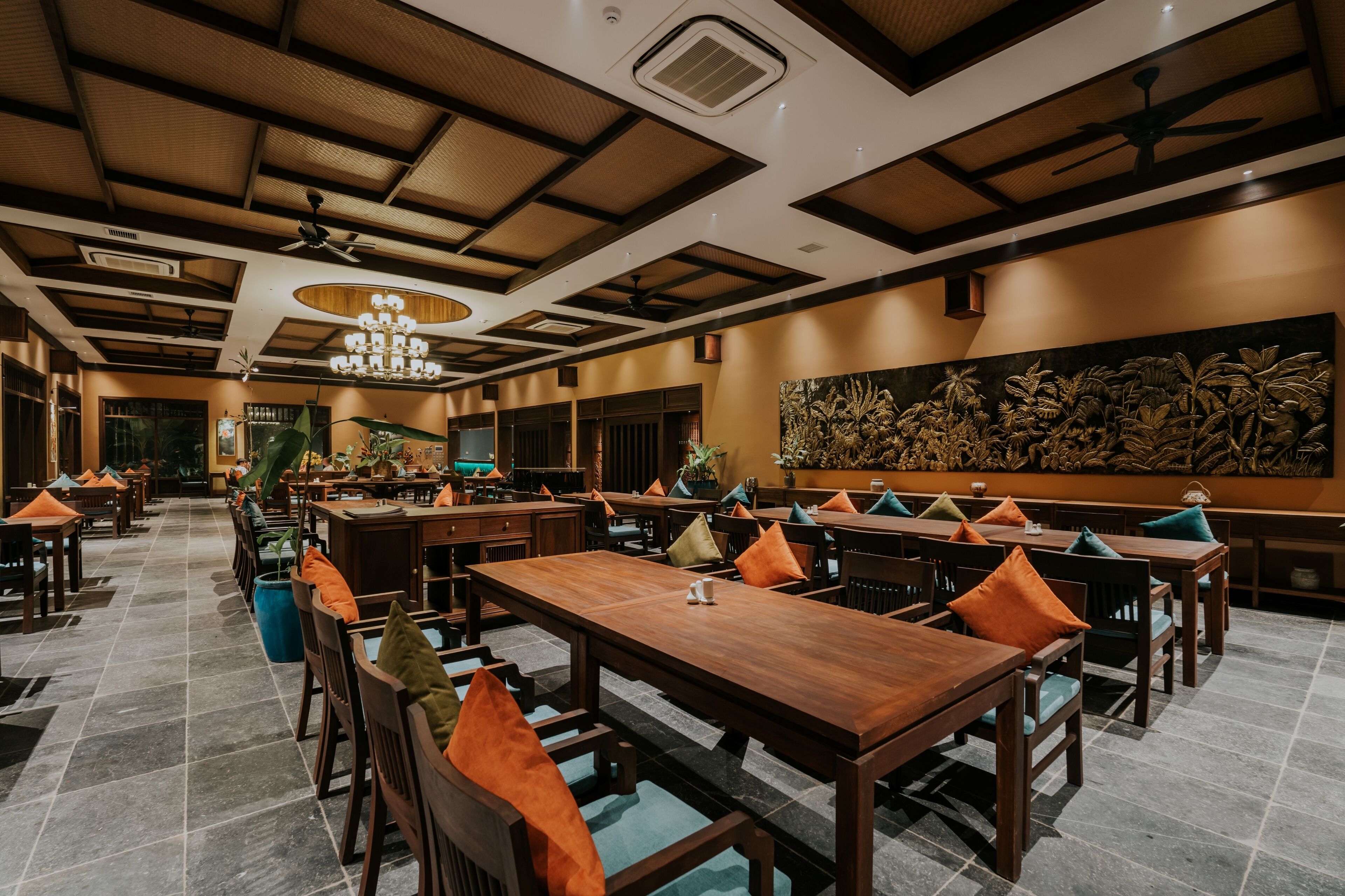 Un restaurant spacieux avec des tables et des chaises en bois, un plafond haut avec un ventilateur et une grande fresque murale.
