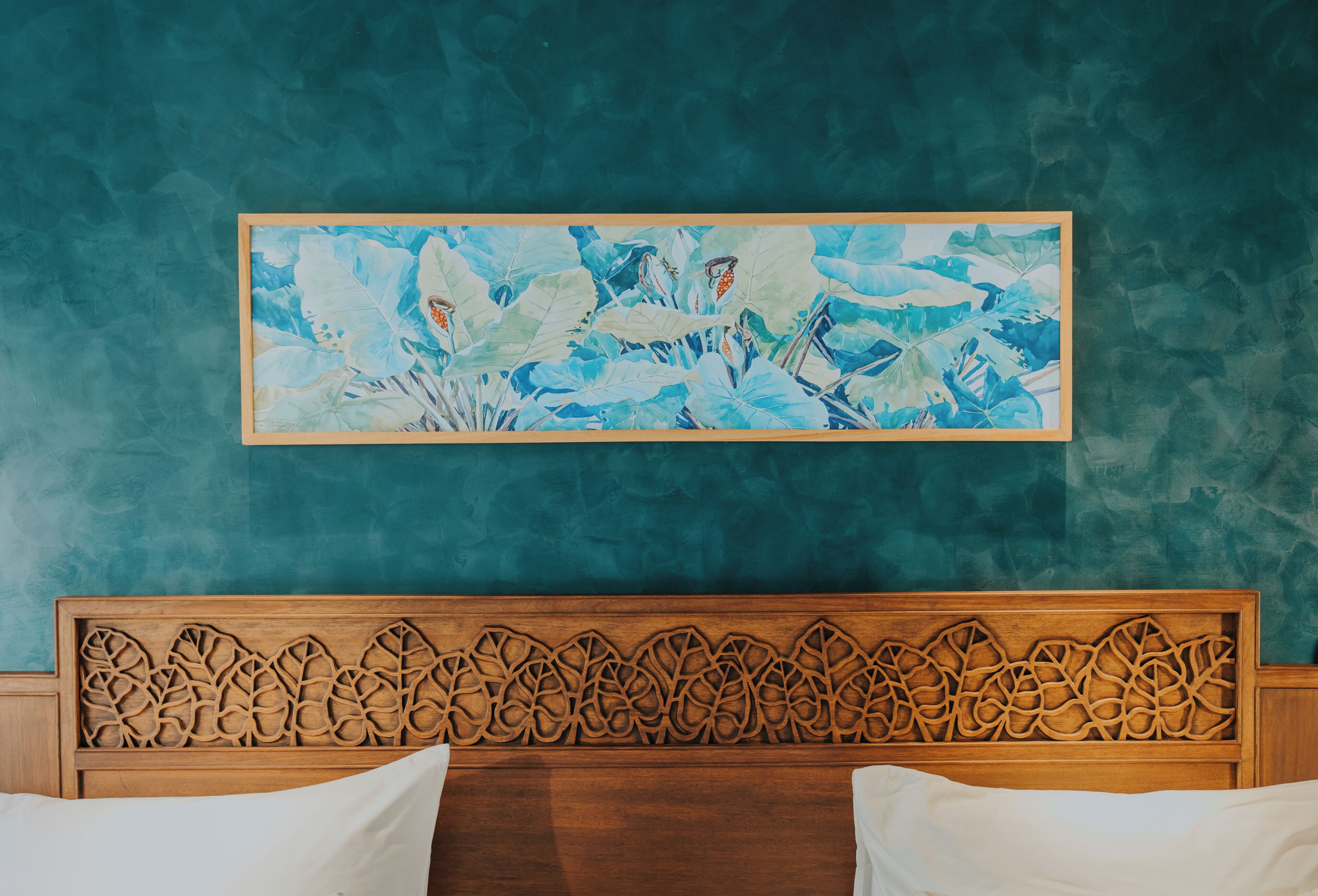 Een slaapkamer met een houten hoofdeinde, een groot abstract schilderij aan de muur en een wand in groenblauwe tint.