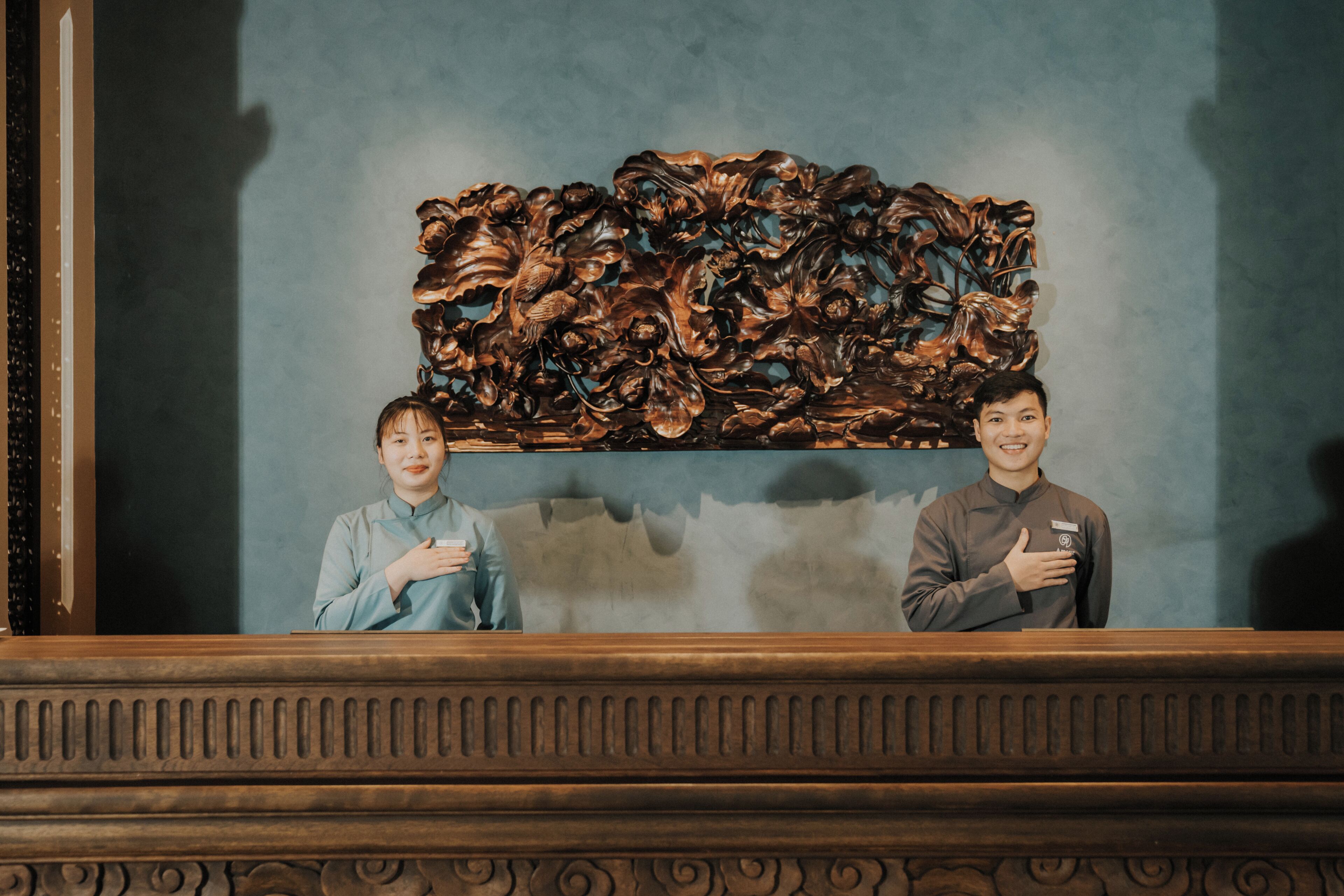 Twee personen staan voor een houten paneel met ingewikkelde gravures.