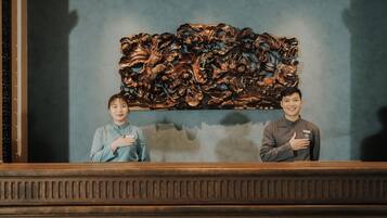 Twee personen staan voor een houten paneel met ingewikkelde gravures.