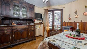 Un comedor con una mesa de madera dispuesta para dos comensales, un aparador grande con puertas de cristal y un televisor montado en la pared.