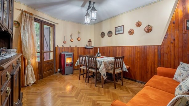 Una habitación acogedora con suelo de madera, una mesa de comedor con sillas, un sofá, un calefactor y un ventilador de techo.
