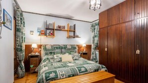 Un dormitorio con una cama de madera, un banco de madera, un armario y una araña.