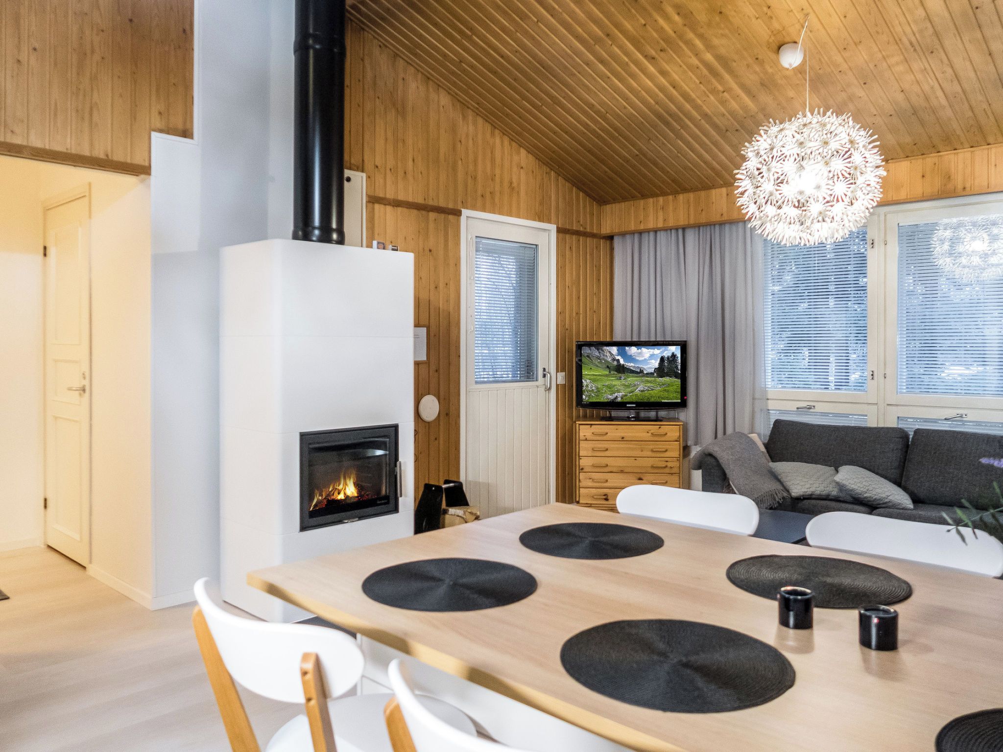 A modern living room with a fireplace, a dining table with chairs, a sofa, and a television.