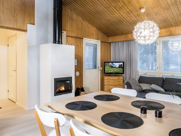 A modern living room with a fireplace, a dining table with chairs, a sofa, and a television.
