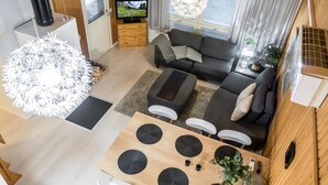Un espai vital modern i compacte amb interior de fusta, una zona de menjador amb taula de fusta i cadires blanques, un sofà gris i una televisió a la cantonada.