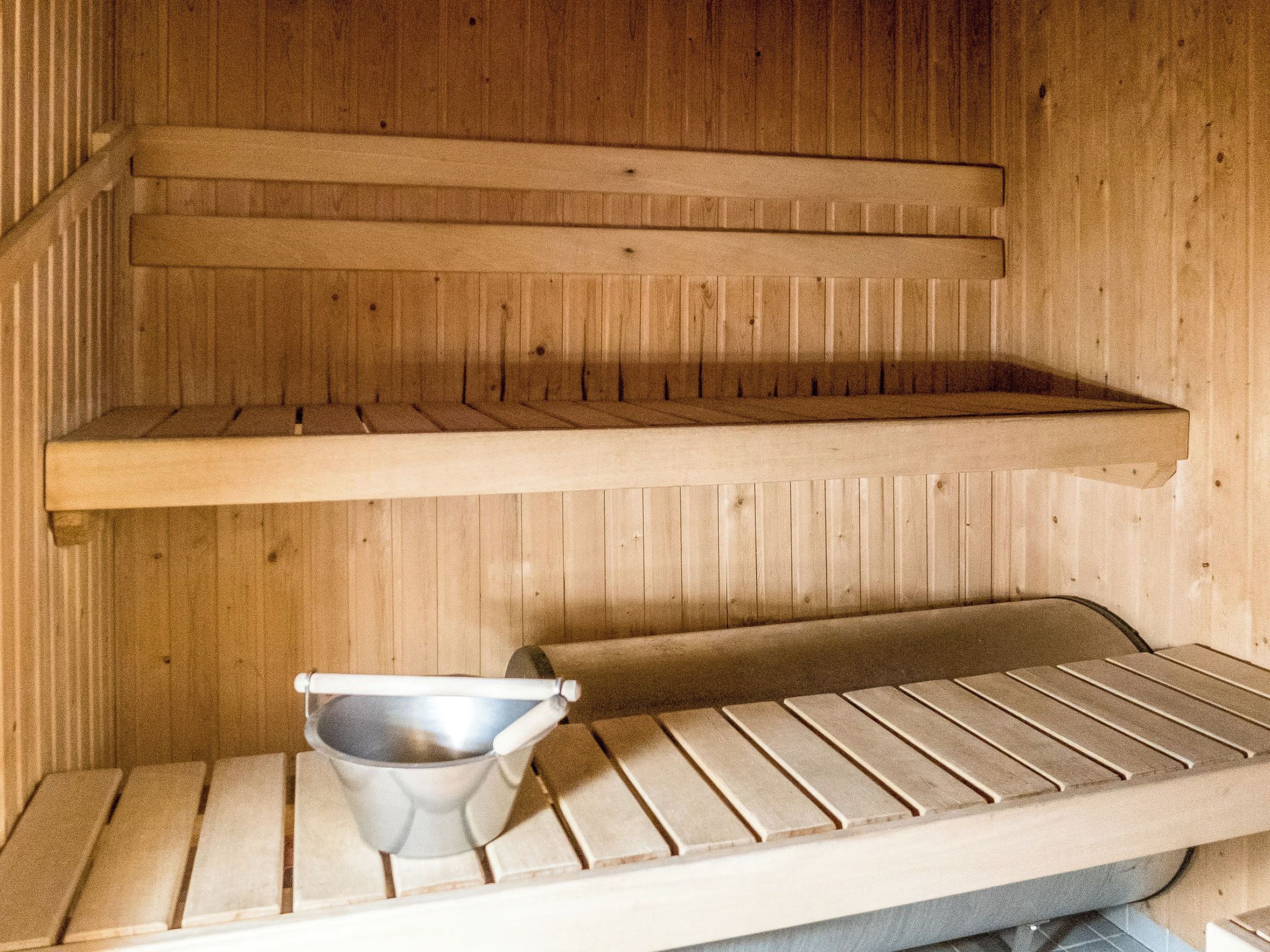 Eine Sauna mit hölzernen Bänken und einem Metallkübel.
