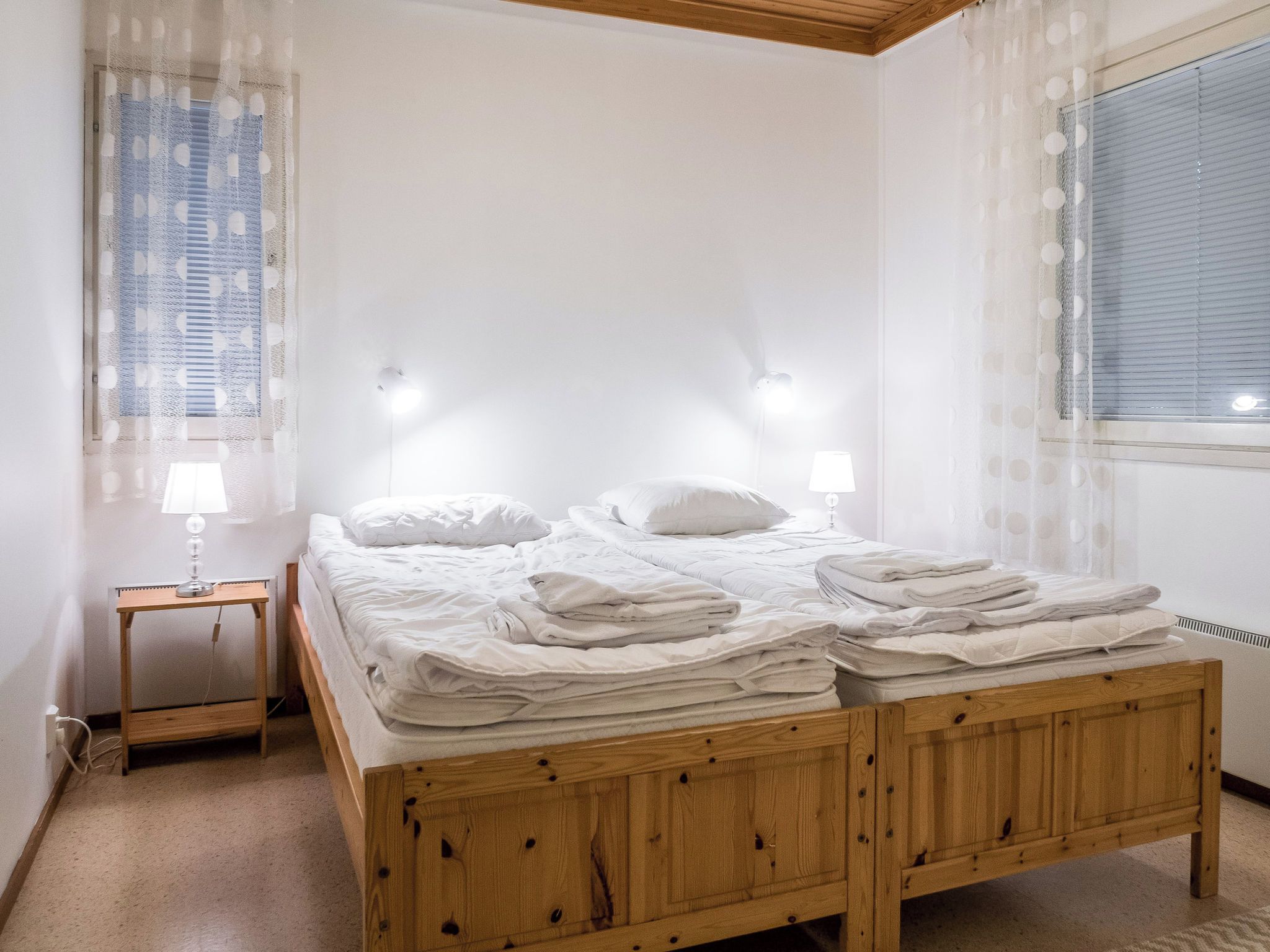 Une chambre à coucher avec un lit en bois, deux tables de chevet, une lampe et une fenêtre avec des rideaux.