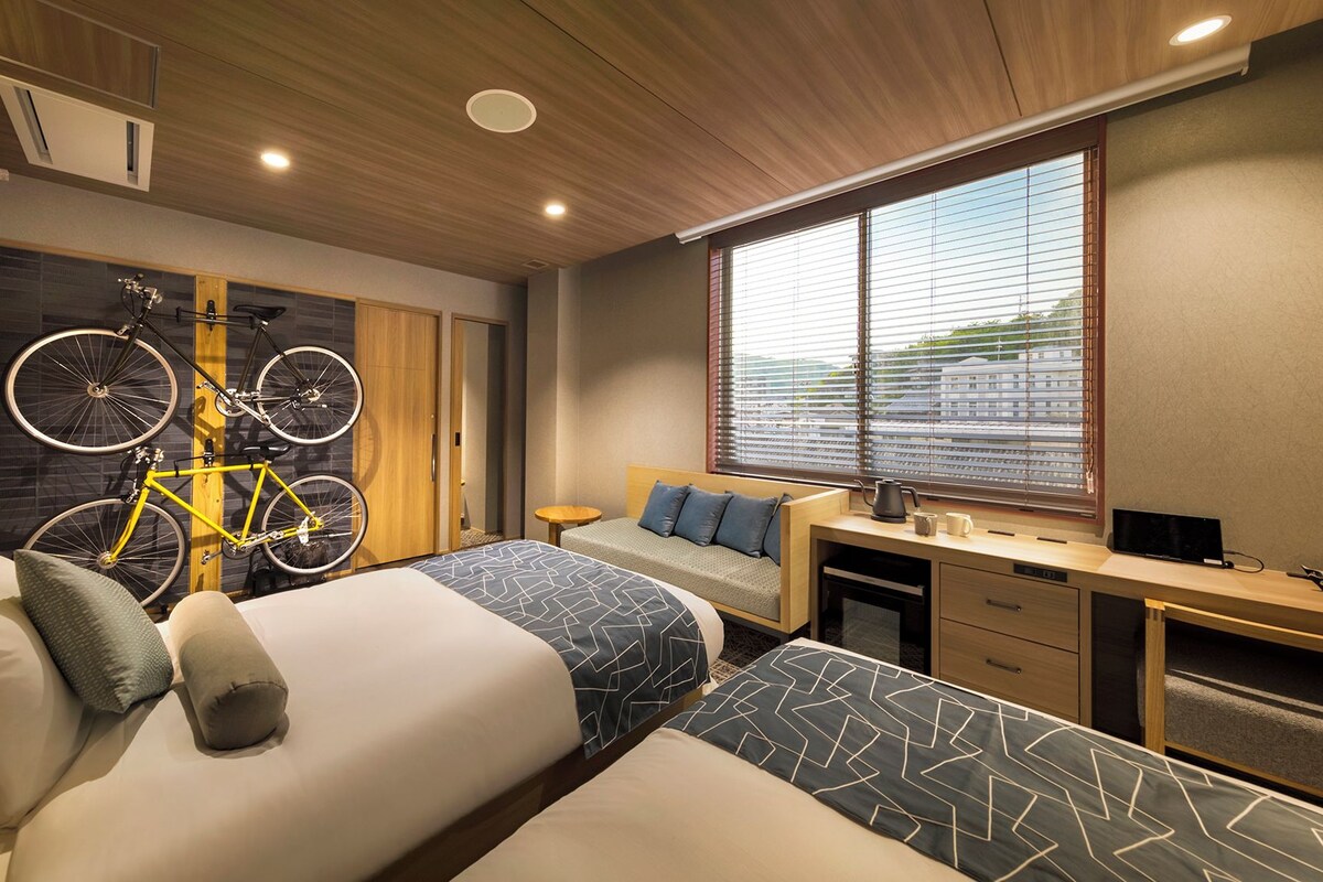 A hotel room with two beds, a desk, and a bicycle mounted on the wall.