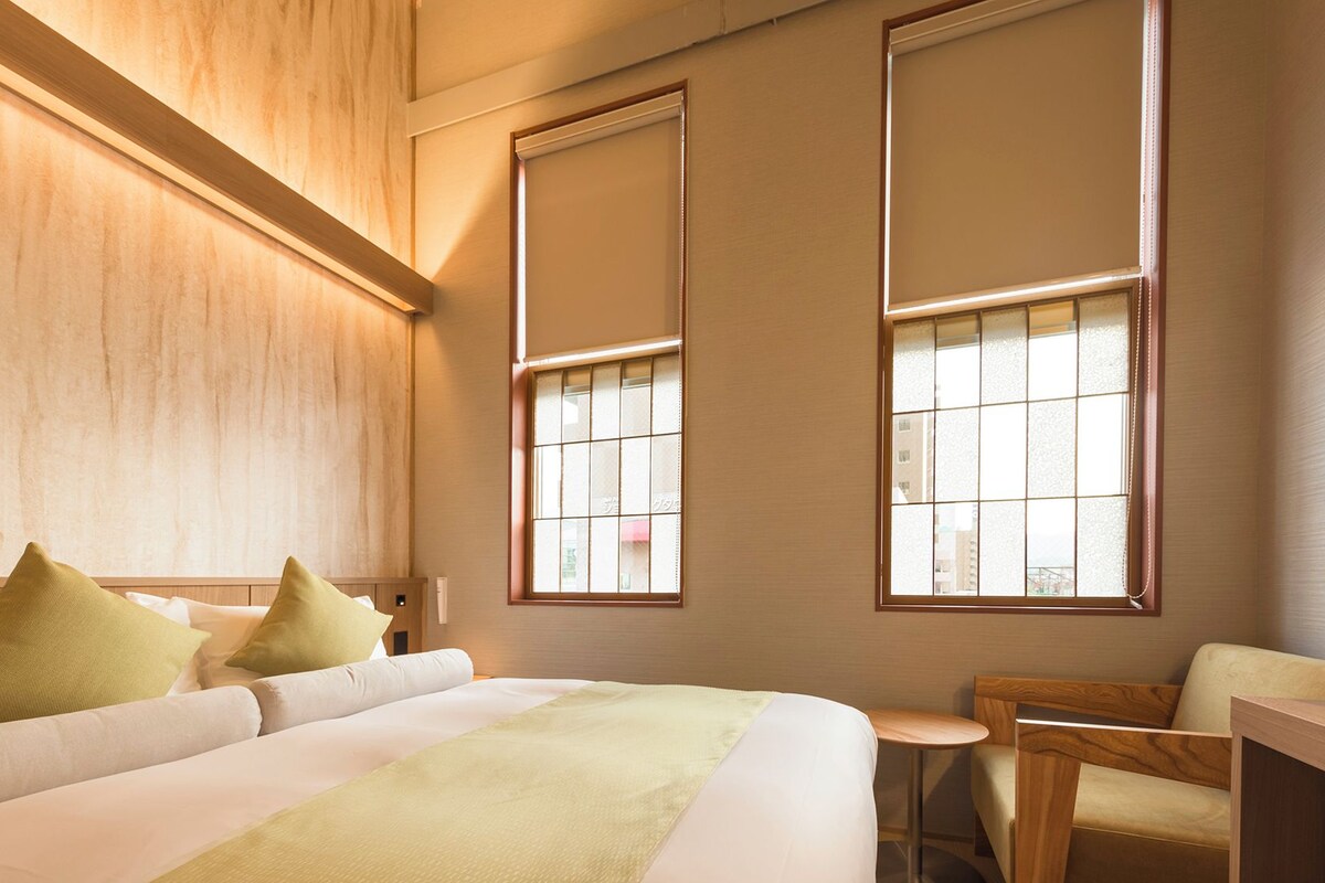 A hotel room with a bed, a desk, and two windows.