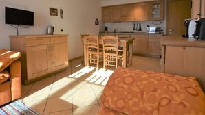 A compact hotel room with a bed, a small kitchenette, a dining area, and a TV mounted on the wall.