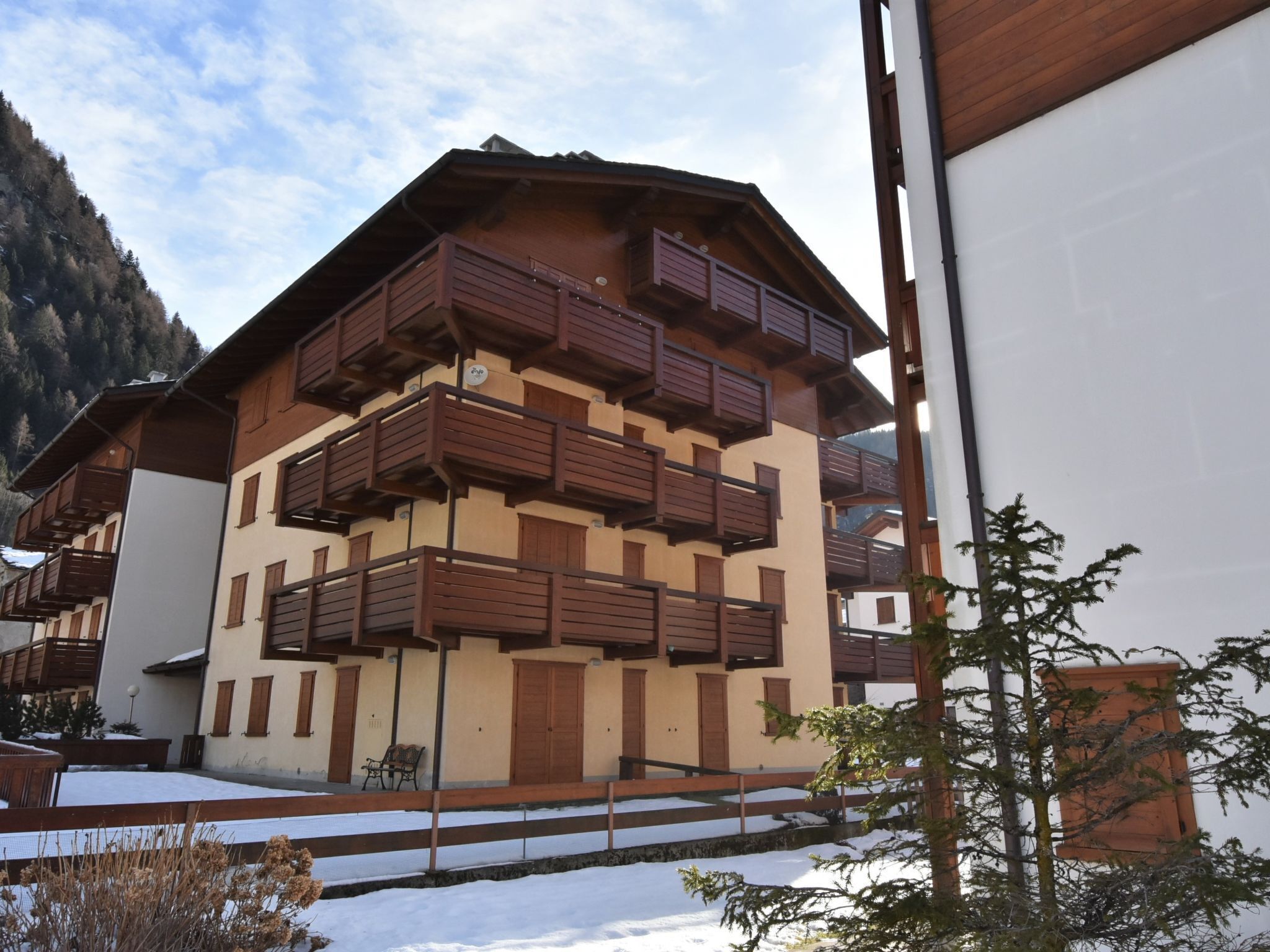 Un chalet à plusieurs étages doté de balcons en bois, un sol recouvert de neige et un paysage montagneux en toile de fond.