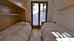A bedroom with two single beds, wooden cabinets, a small rug, and a door leading to a balcony.
