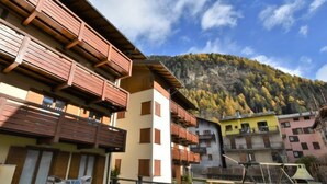 A multi-story building with wooden balconies, a courtyard with outdoor seating, and a mountainous backdrop.