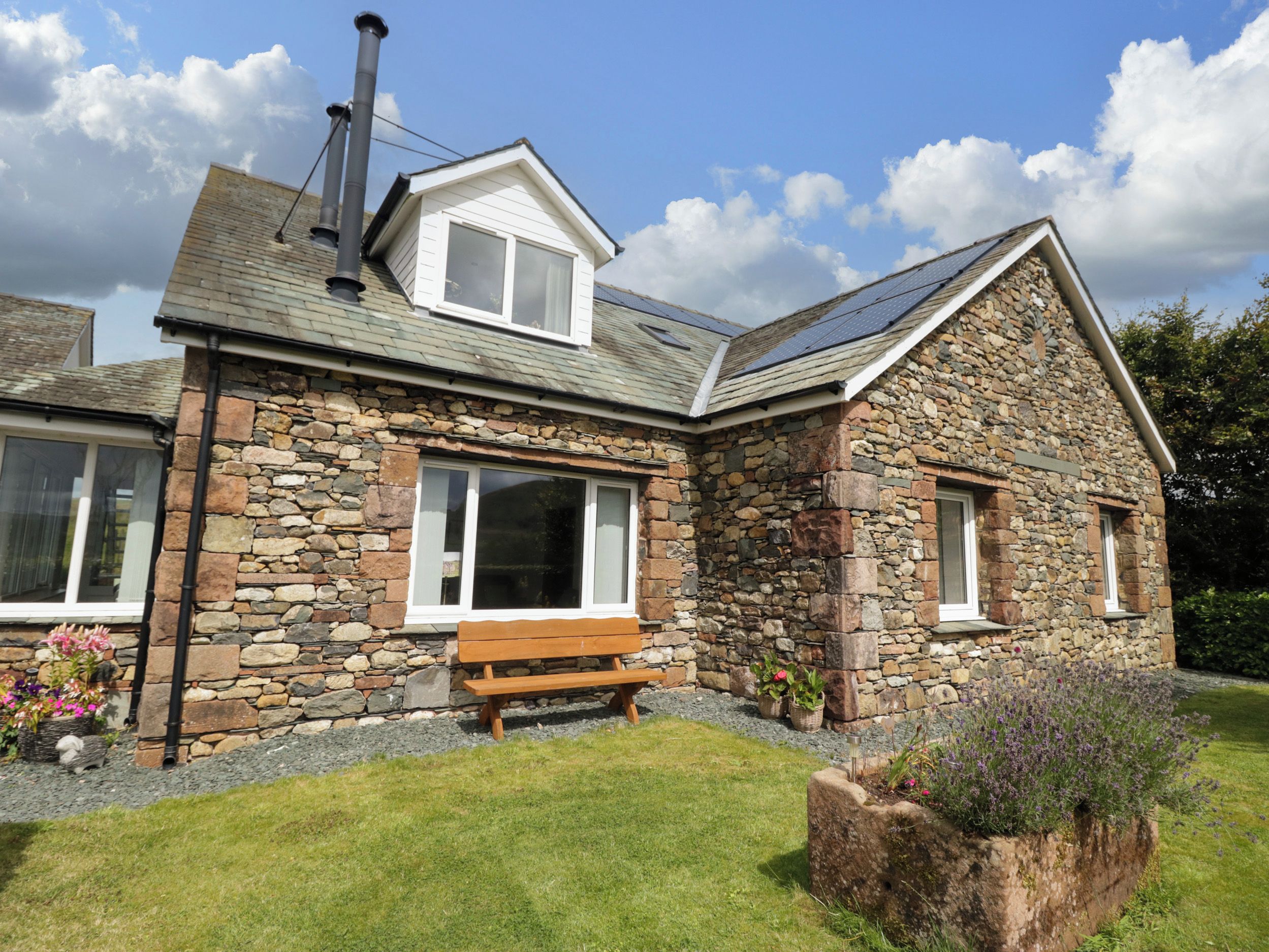 A stone house with a sloped roof, a chimney, and a bench in the front yard.