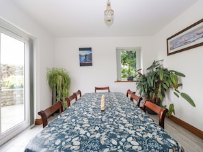 A dining area with a table set for four, surrounded by chairs, with a large potted plant on the right and a window with a view of greenery. - Sherriff (Penrith)