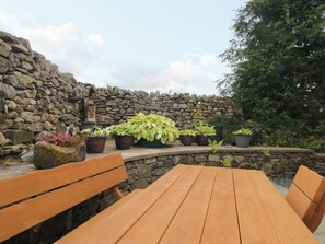 A stone wall with potted plants and a wooden bench. - Sherriff (Penrith)