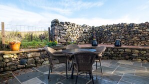 Une terrasse avec des murs en pierre, des chaises en osier, une table et des luminaires d’extérieur.