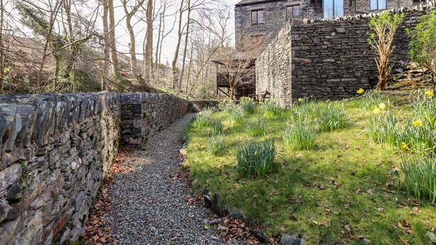 A stone wall leading to a grassy area with daffodils and a stone building with a stone facade. - Ghyll View (Ambleside)