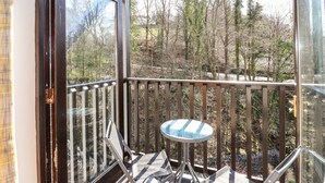 A balcony with a glass door, a small round table, and a chair. - Ghyll View (Ambleside)