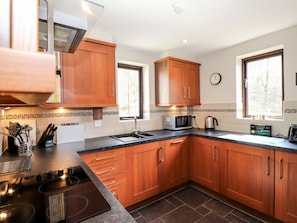 A modern kitchen with wooden cabinets, a microwave, a kettle, and a window with a view of trees. - Ghyll View (Ambleside)