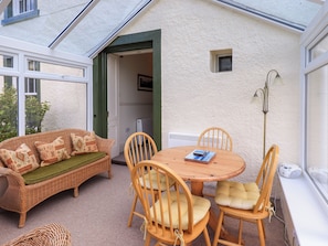A cozy outdoor seating area with a wicker sofa and wooden chairs, a round table, and a lamp. - Sandburne Cottage (Keswick)