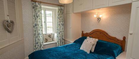 Un dormitorio con cama, ventana con cortinas, lámpara de pared y cabecera de madera.