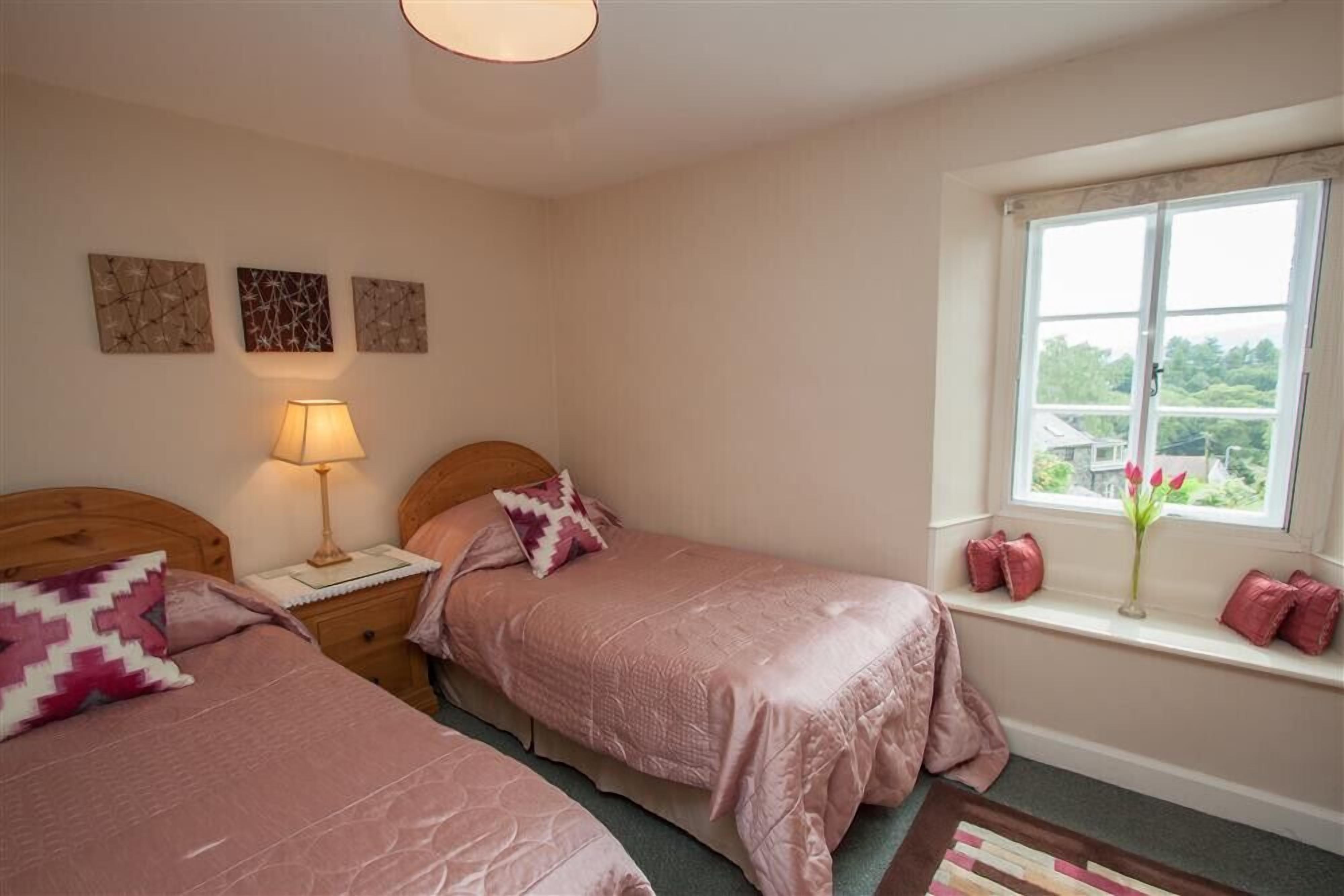 Une chambre avec deux lits, une table de chevet, une lampe et une fenêtre donnant sur un beau paysage.
