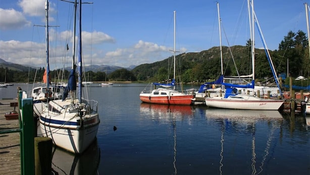 Un port de plaisance où sont amarrés plusieurs voiliers, avec une eau calme et un paysage montagneux en arrière-plan.