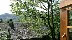 Ein Gebäude aus Stein mit Ziegeldach, umgeben von Grünflächen und Bergen im Hintergrund.
