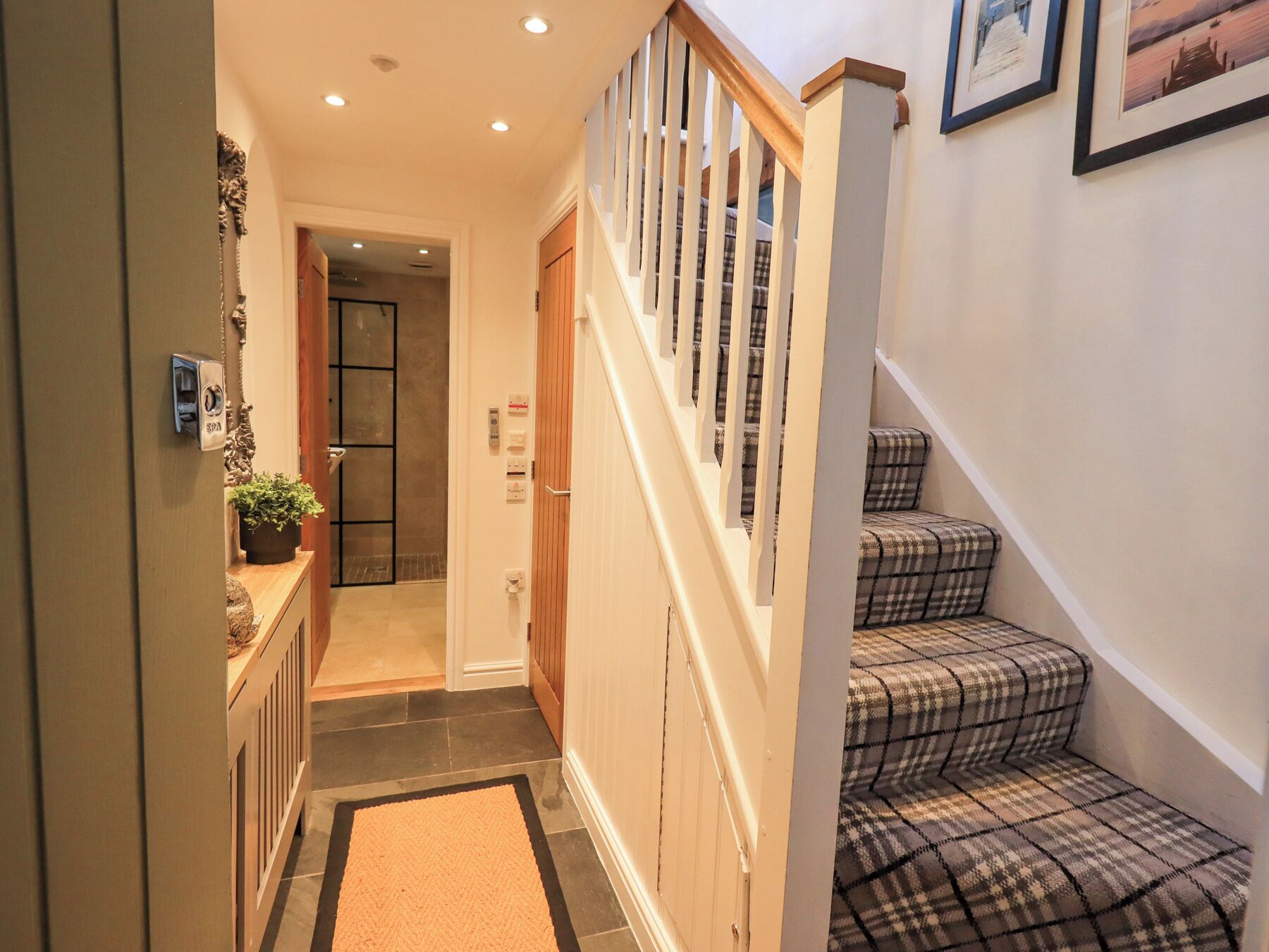 A hallway with a wooden staircase, a door with a lock, and a small plant on a counter.
