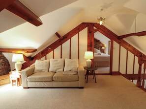 An attic bedroom with a sloped ceiling, exposed wooden beams, a sofa, two bedside tables with lamps, and a bed with a headboard. - High Raise (Ambleside)