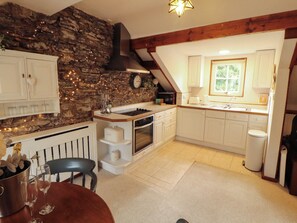 A kitchen with white cabinets, a stone wall, a wooden ceiling, and a window. - High Raise (Ambleside)