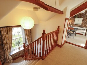 A staircase with wooden balusters leading to a landing with a view of a stone wall and a dining area. - High Raise (Ambleside)