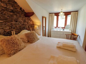 A bedroom with a stone wall, a bed with fluffy pillows, a dresser, and a chandelier. - High Raise (Ambleside)