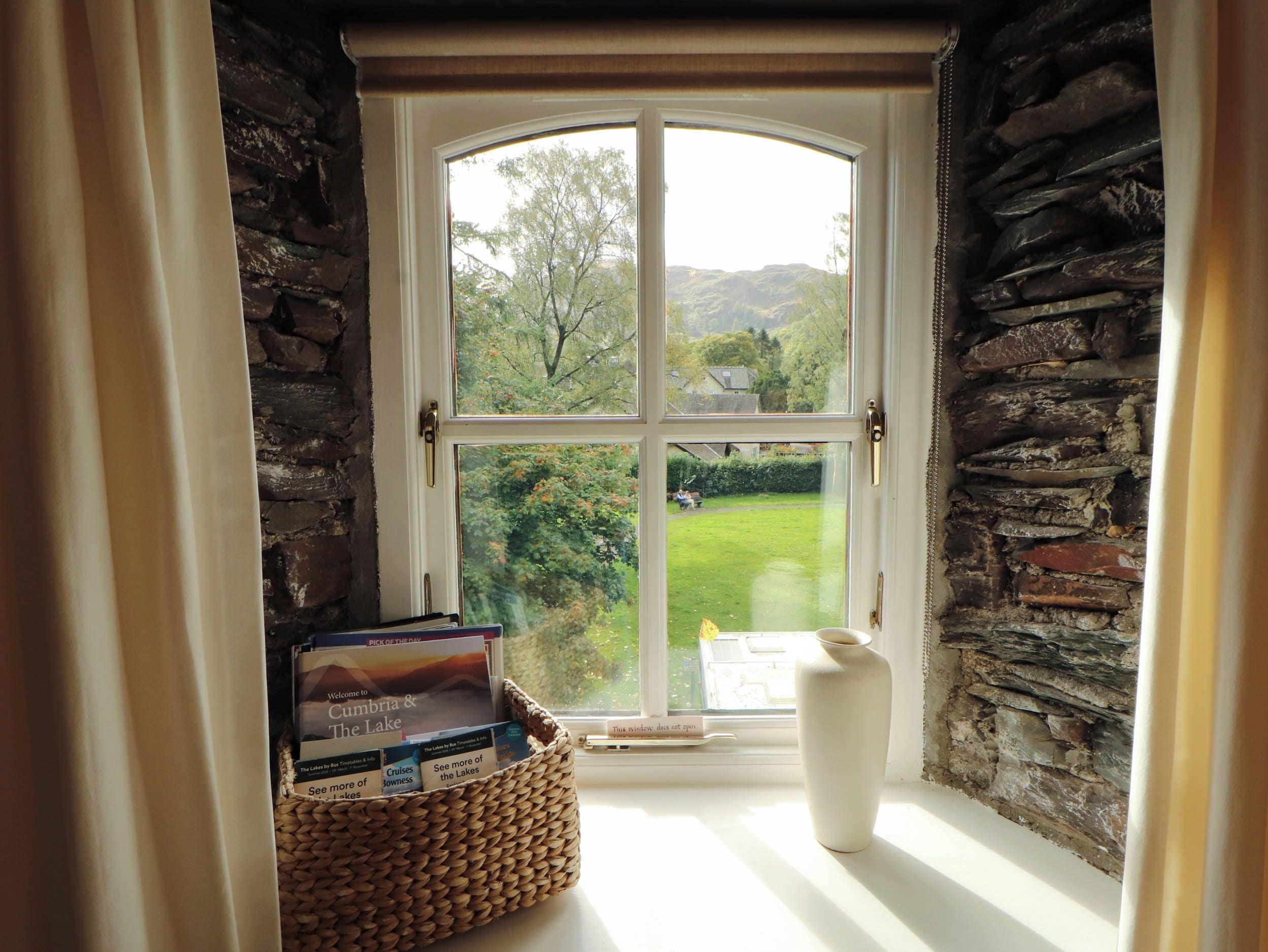 A room with a large window, a wicker basket with books, and a white vase on the windowsill.