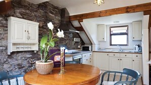 Una cocina con armarios blancos, pared de piedra y techo de madera.