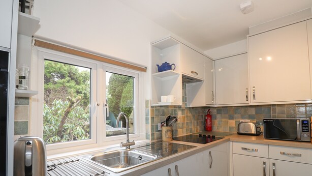 A modern kitchen with a stainless steel sink, a kettle, a toaster, and a microwave. - Larch Cottage (Ambleside)