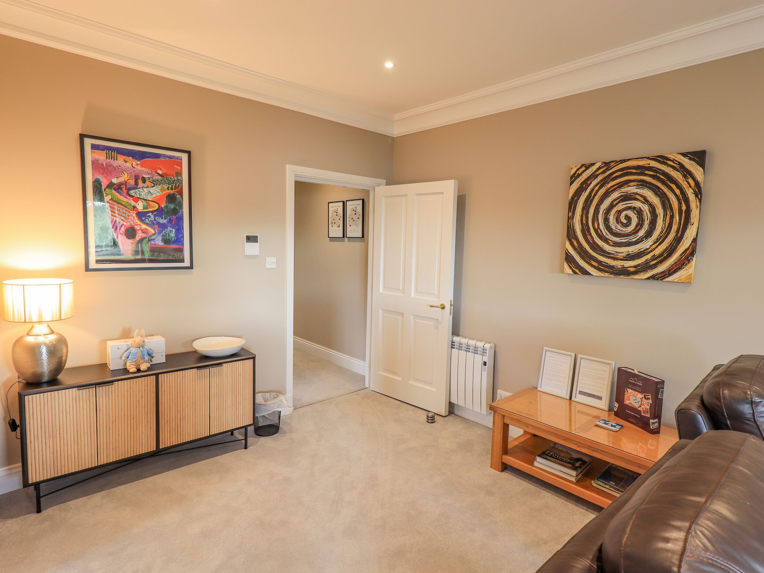 A living room with a beige carpet, a wooden console table, a leather couch, a white door, and a radiator.