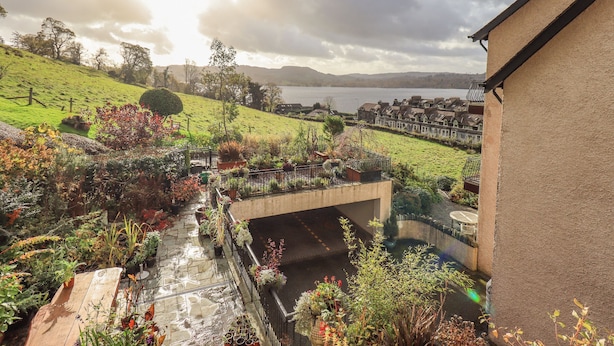 A residential area with a view of a lake, a green hill, and terraced houses in the background.