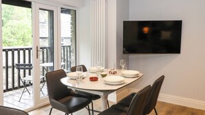A dining area with a table set for four, a TV mounted on the wall, and a sliding glass door leading to an outdoor patio. - Jenever Cottage (Ambleside)