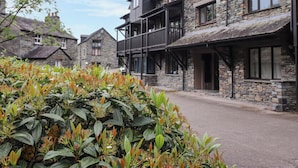 A stone building with a balcony, a small garden with green and orange foliage, and a clear sky. - Jenever Cottage (Ambleside)