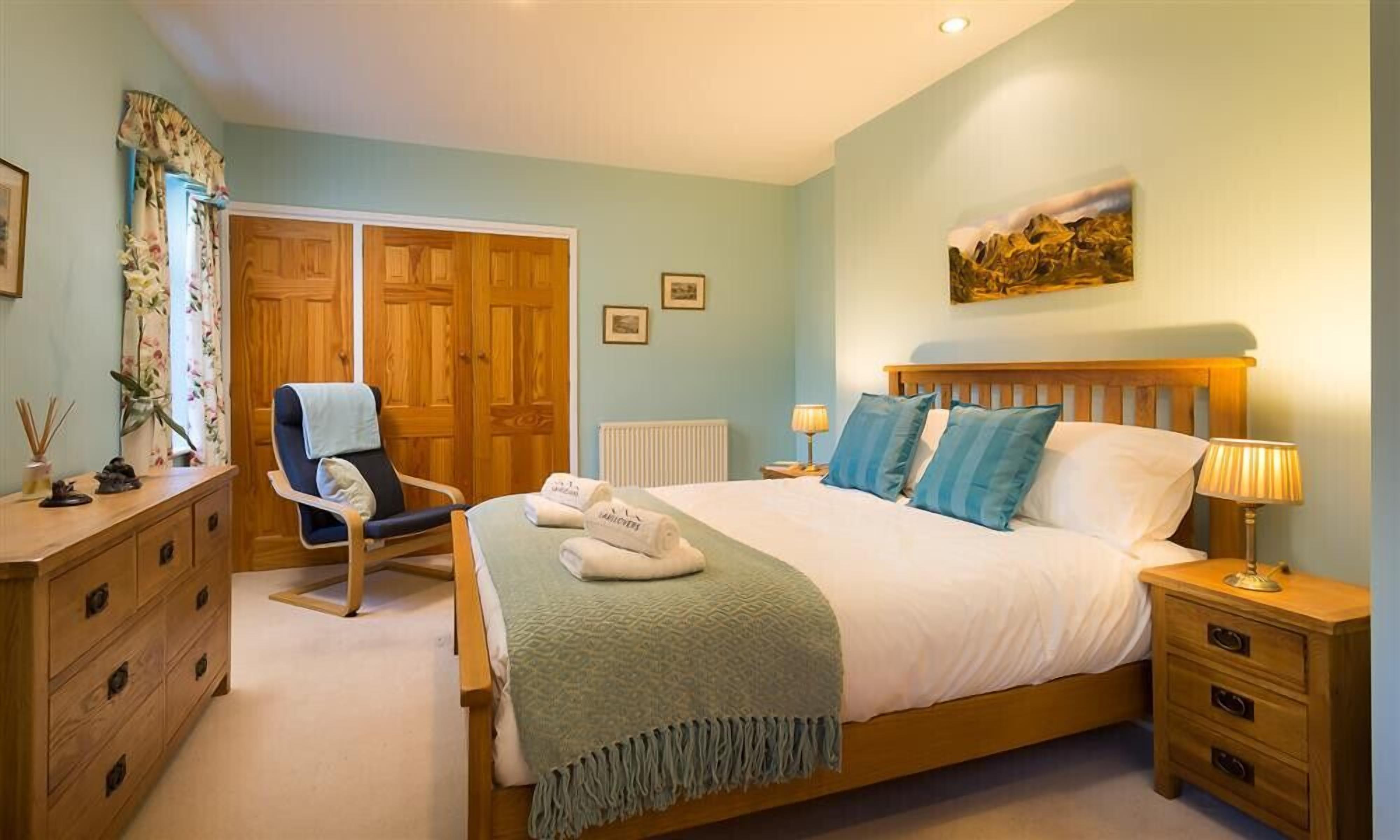 A bedroom with a bed, a chair, a dresser, a nightstand, and a painting on the wall.