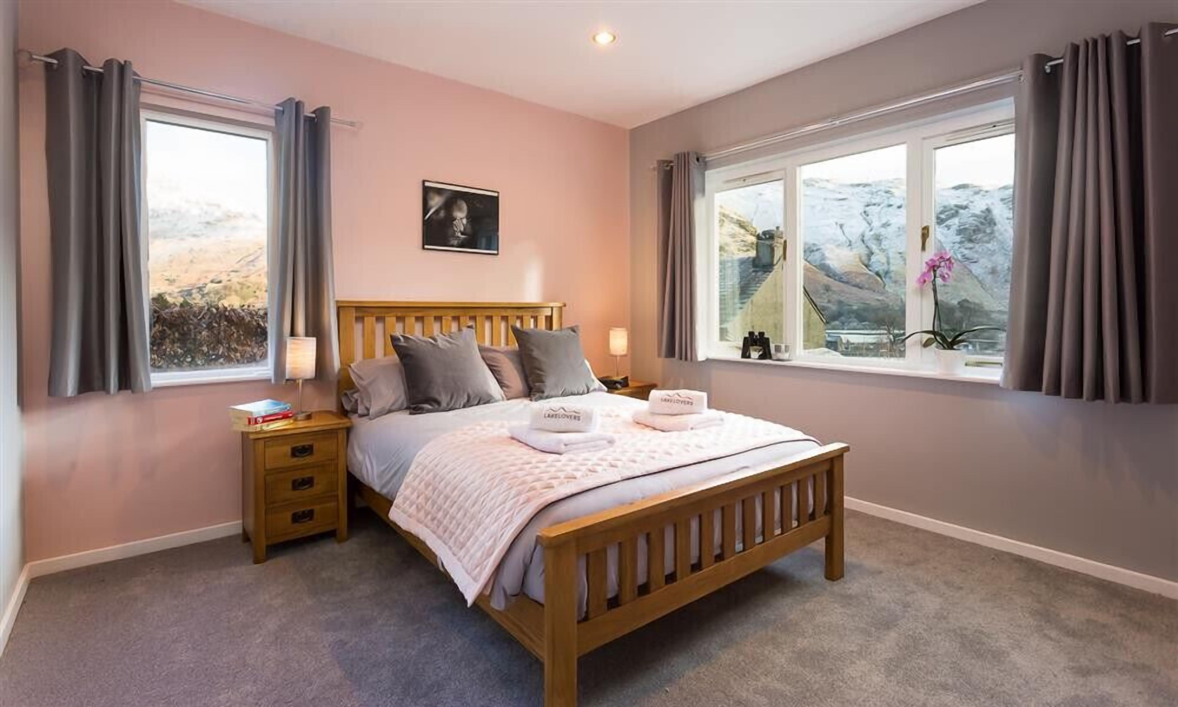 A bedroom with a wooden bed, two bedside tables, a night lamp, a framed picture, and a window with curtains.