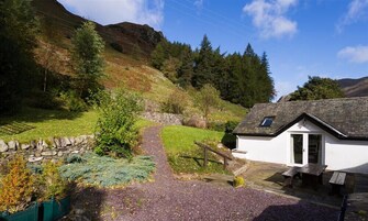 Uma casa de campo branca com telhado de pedra, um pequeno alpendre e um banco de madeira.