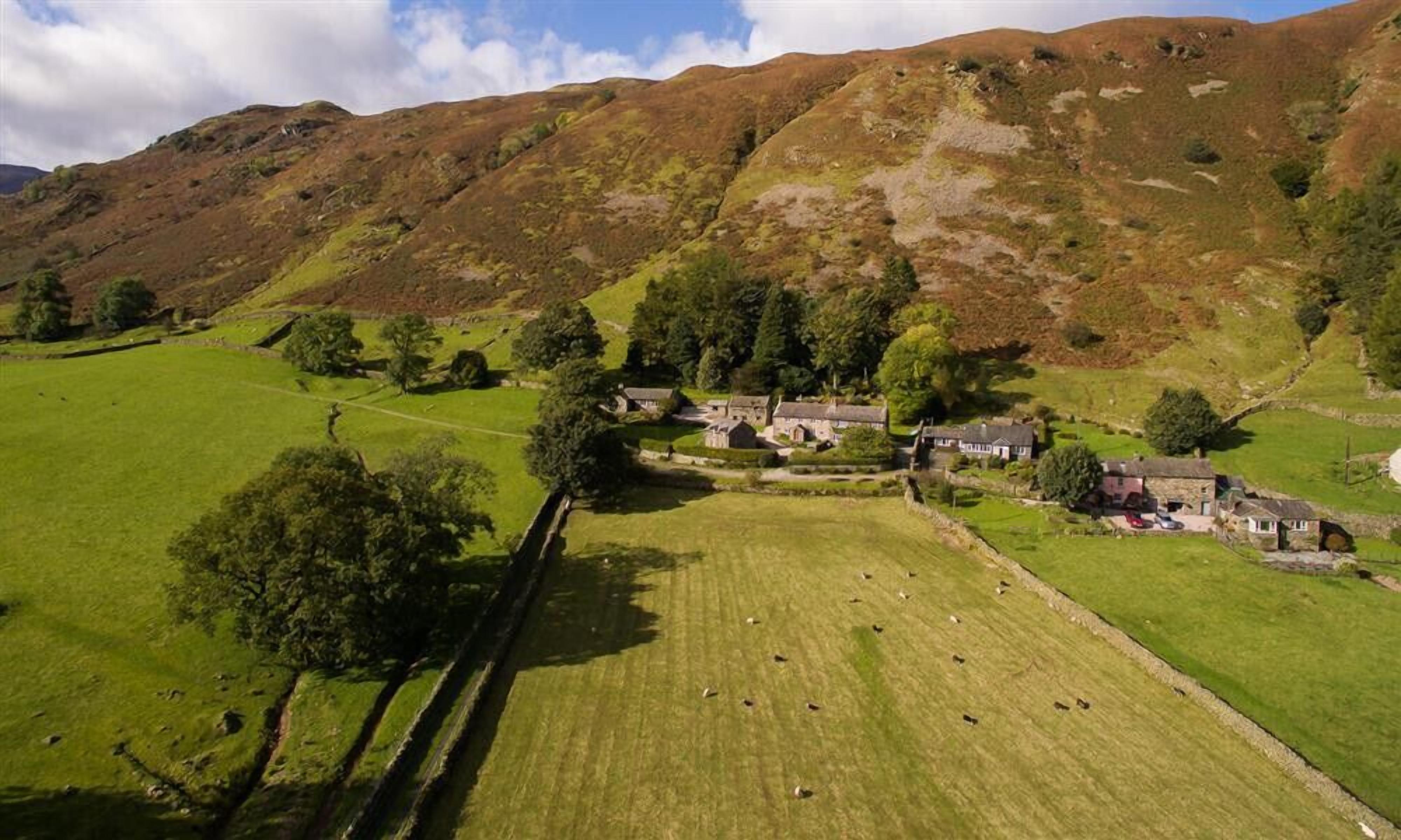 A rural landscape with a cluster of stone buildings surrounded by green fields and trees.